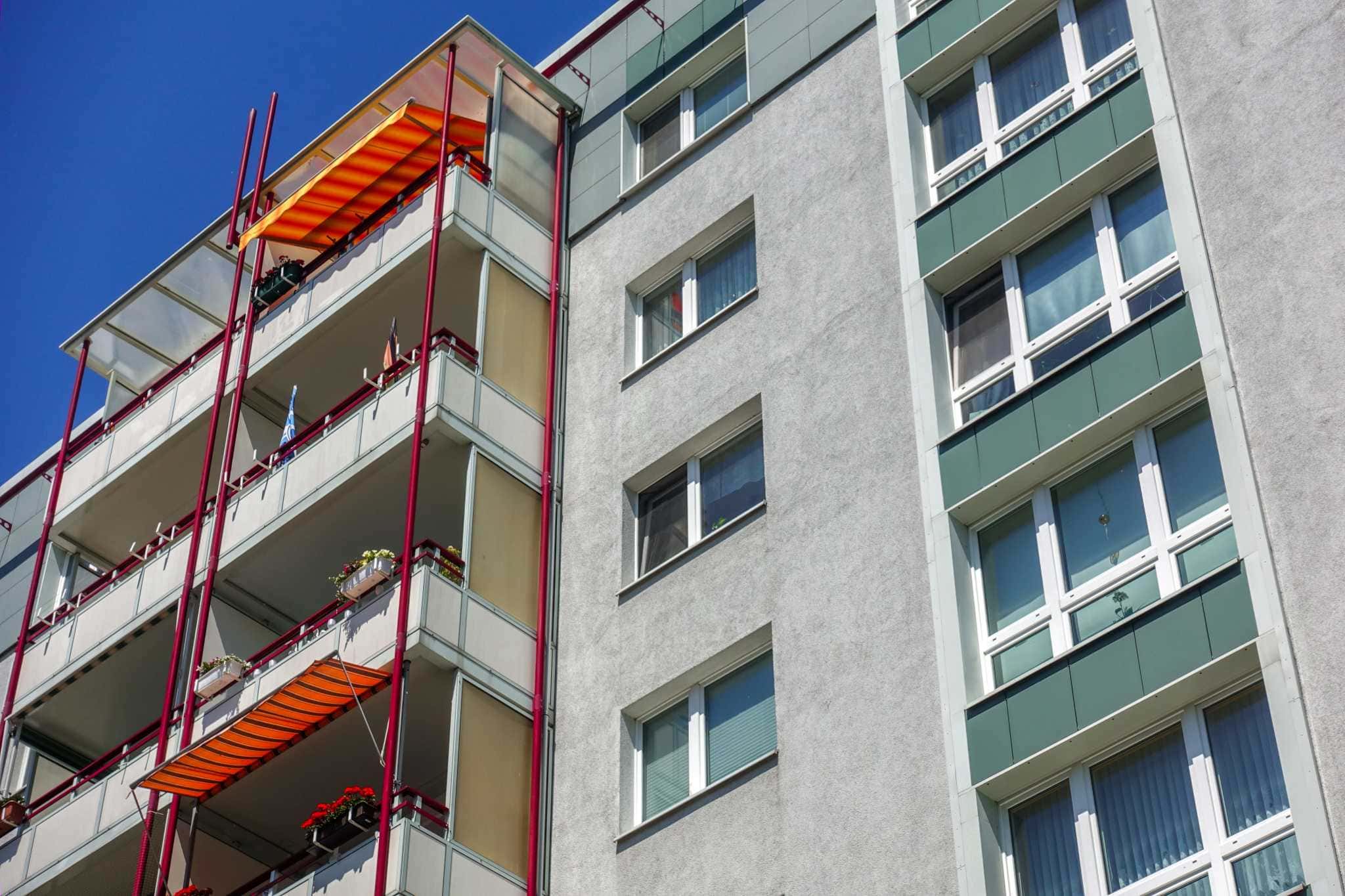 Mehrfamilienhaus mit sanierungsbedürftiger Fassade und Balkonen, teilweise mit Markisen ausgestattet.
