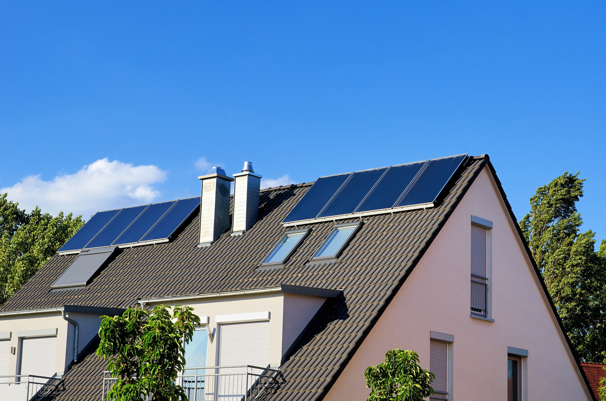 Modernisiertes Einfamilienhaus mit dunklem Satteldach und installierten Solarthermie- und Photovoltaikmodulen – Symbol für ein energieeffizientes Gebäude mit erneuerbarer Energieversorgung.