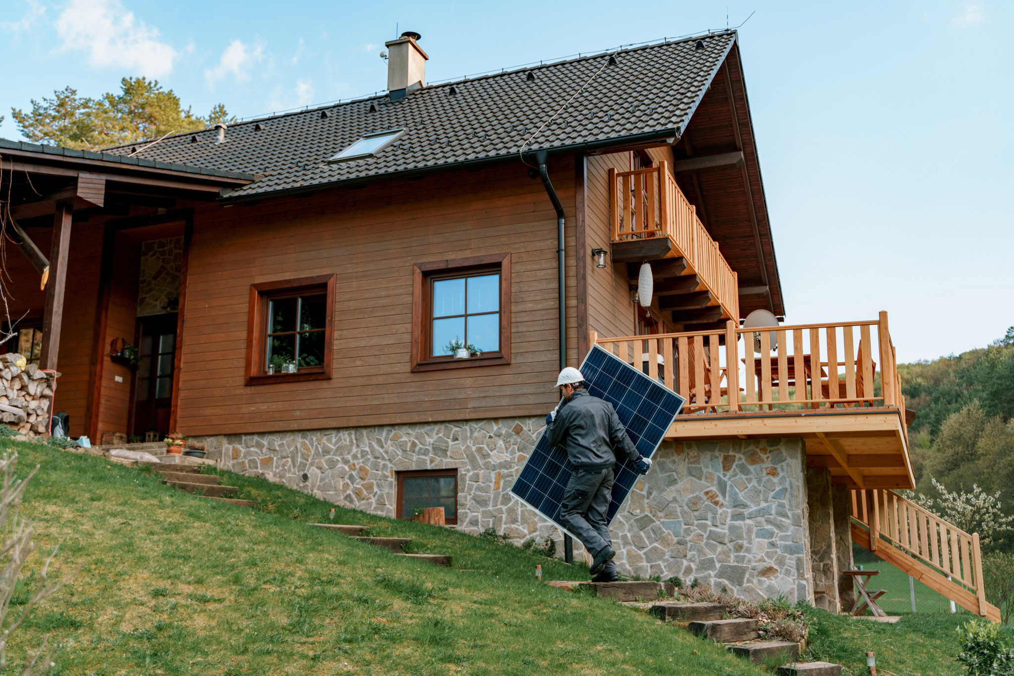 Bauarbeiter trägt Solarpanel zu einem Holzhaus.